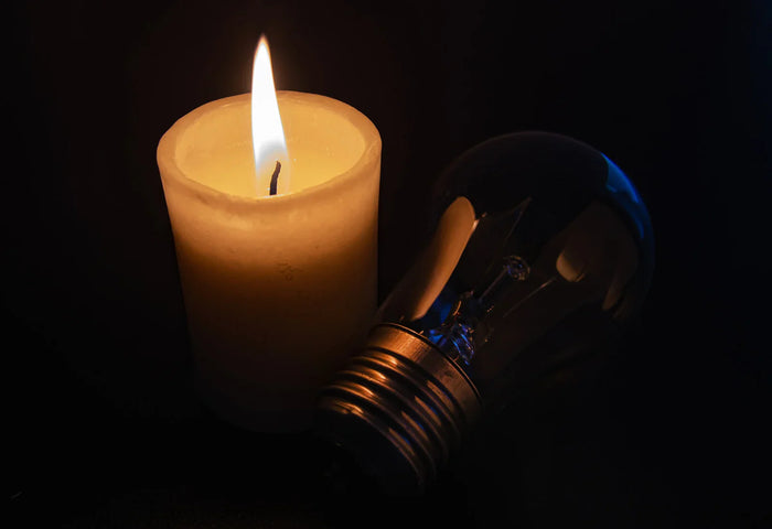 A lit candle next to a dead lightbulb