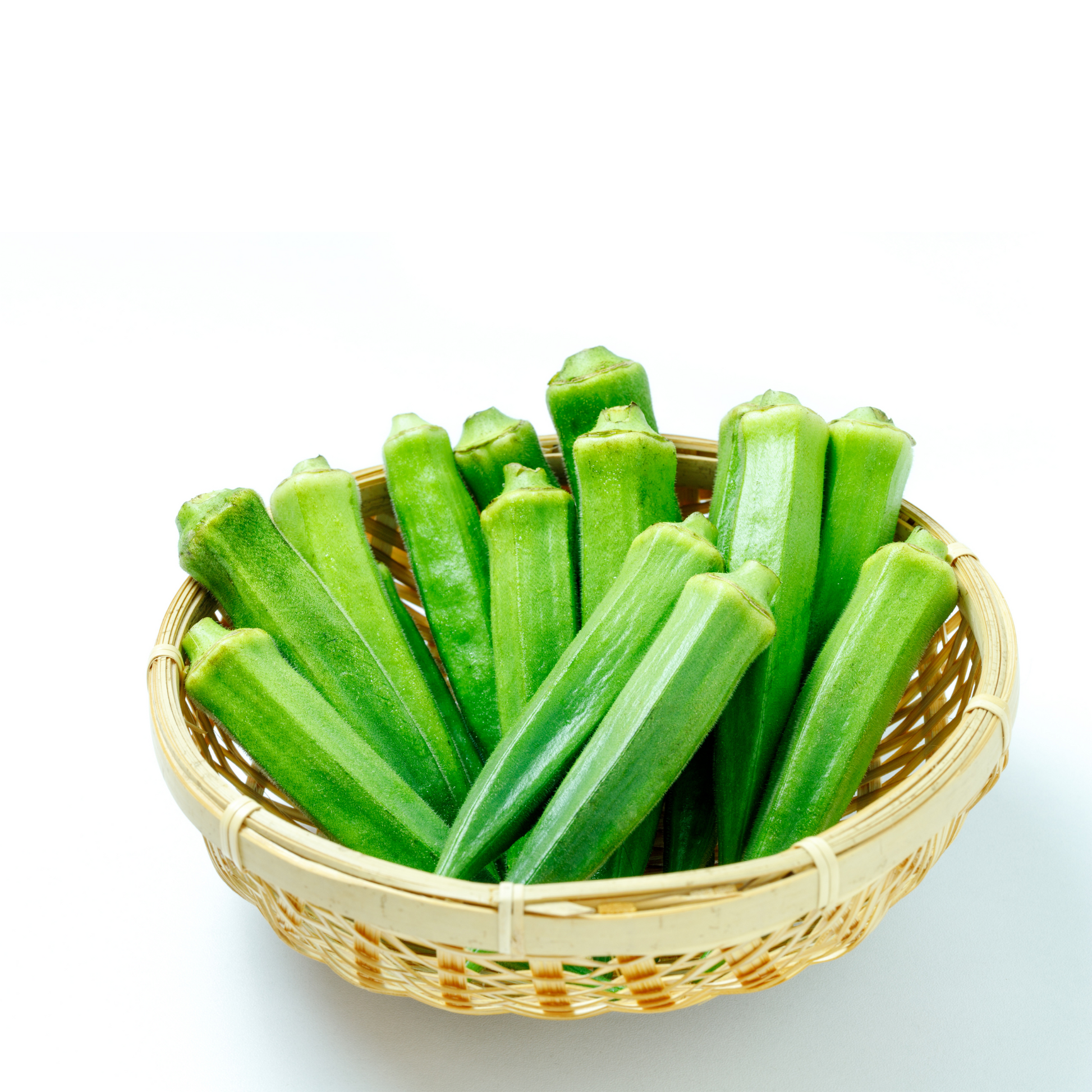 Basket filled with fully-grown Clemson Spineless Okra pods on a white background