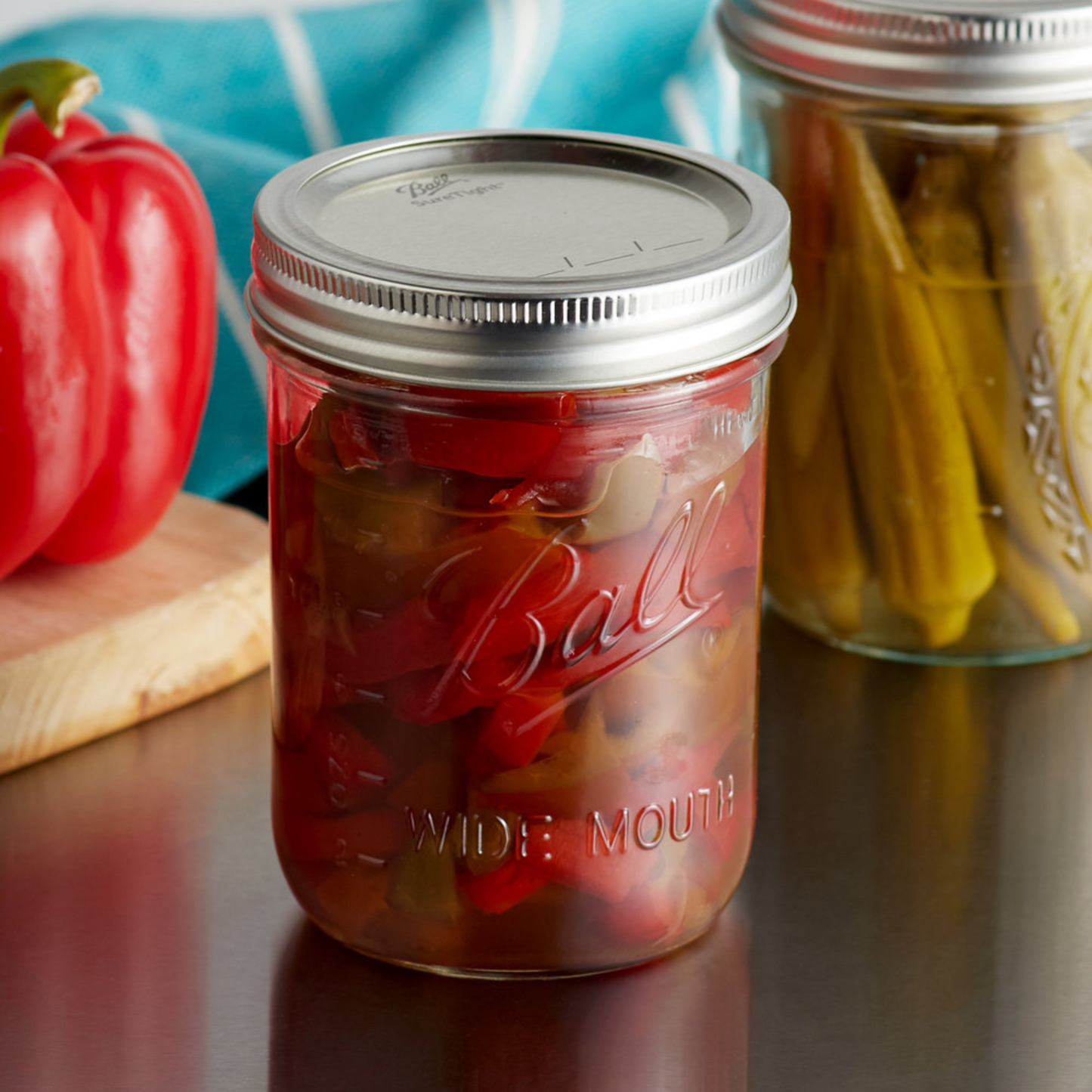 Two wide mouth Ball mason jars filled with a colorful mix of pickled peppers and cucumbers